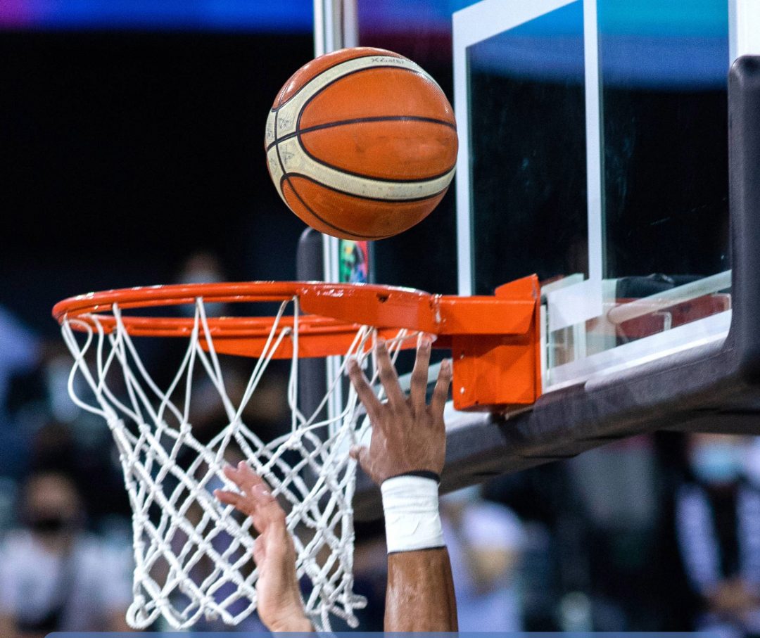 Basketball kurz vor dem Korb, zwei Hände zum Korb gestreckt